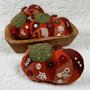 A completed Wool Felt Crazy Quilt Pumpkin Pattern from the Posy Collection displayed in a wooden bowl on a table.